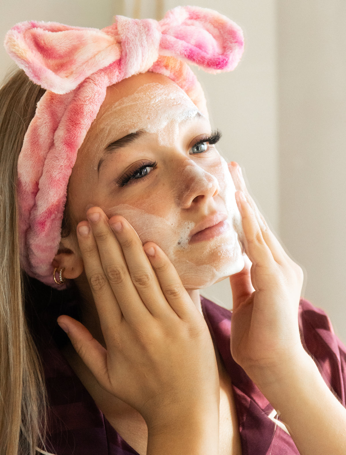 Teenage girl applying facial foamy cleanser with pink bow headband on head