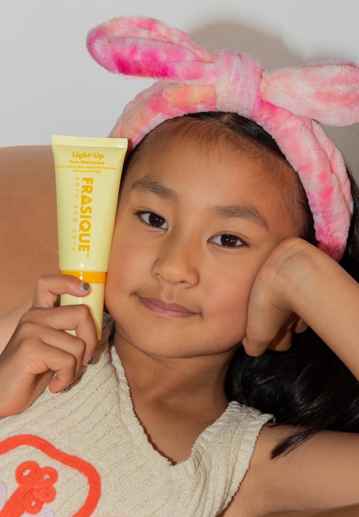 Child wearing a pink headband with bunny ears holding a Frasique product.