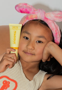 Child wearing a pink headband with bunny ears holding a Frasique product.